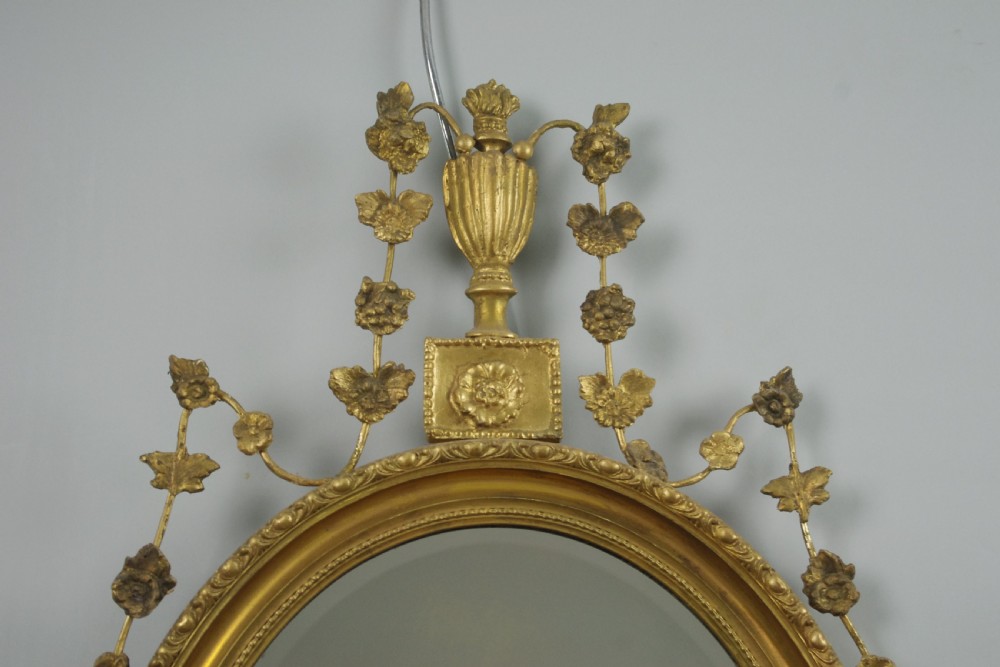 A Victorian oval wall mirror featuring a gilded frame embellished with beaded moulding, an urn finial, and delicate leaf garlands. View II