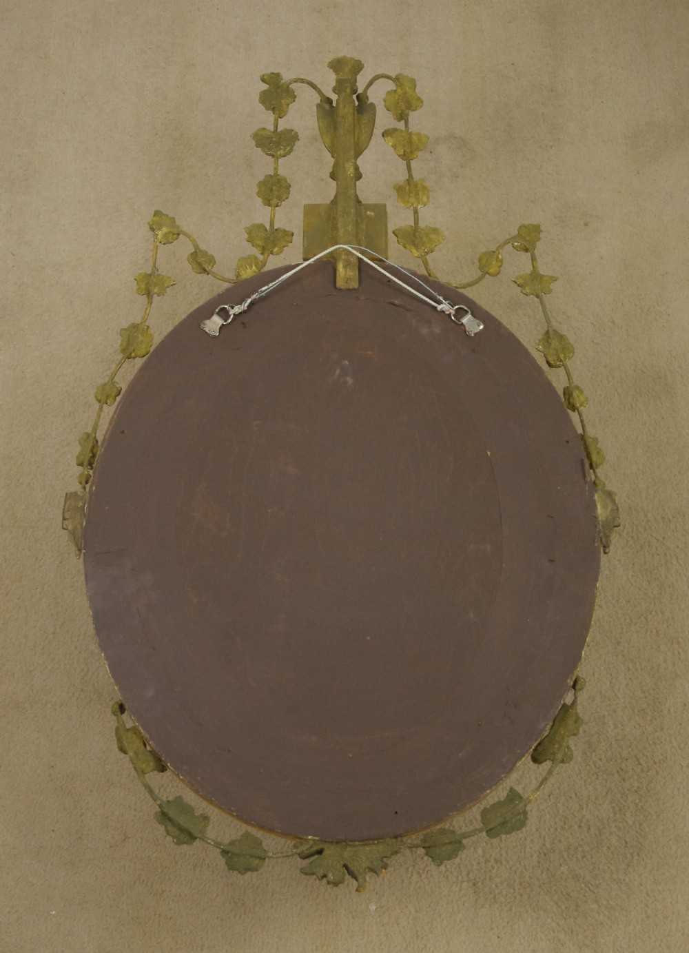 A Victorian oval wall mirror featuring a gilded frame embellished with beaded moulding, an urn finial, and delicate leaf garlands. View VII