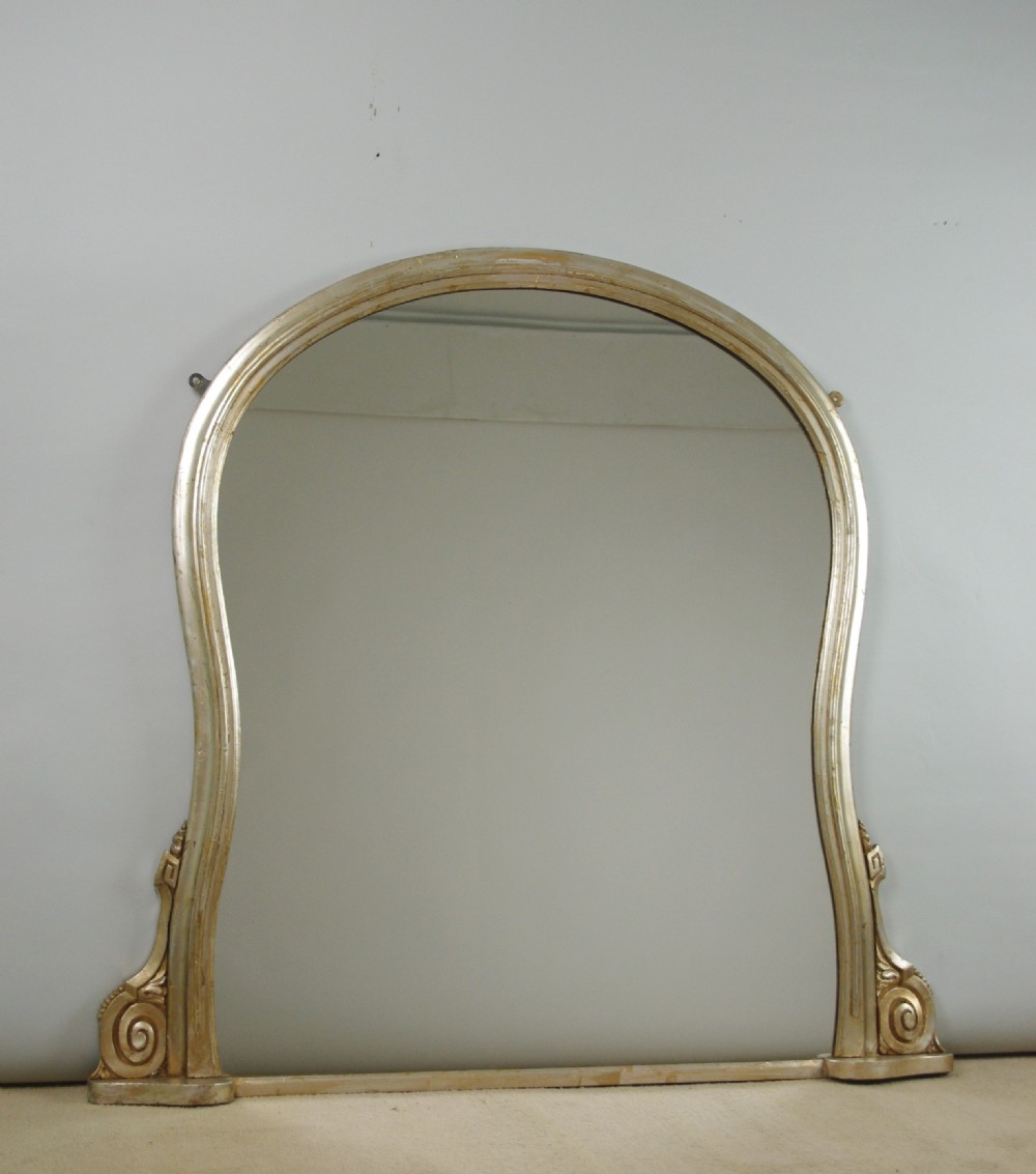 A Victorian silvered overmantel mirror featuring an arched upper frame, molded detailing, and decorative scroll motifs at the base.