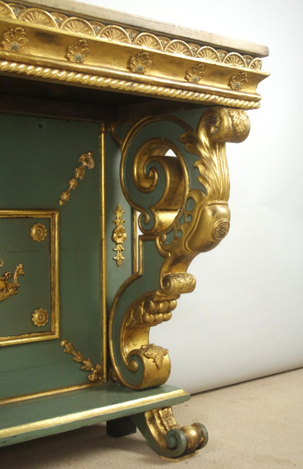 A 19th-century French console table with a cream marble top, green painted base, gilding, and large scroll legs. View XII