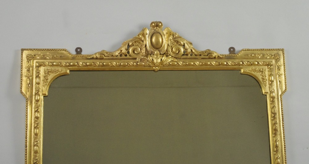 A large Victorian gold leaf gilt overmantel mirror featuring an ornate central crested cartouche, moulding, scroll feet, and arched upper corners. View II
