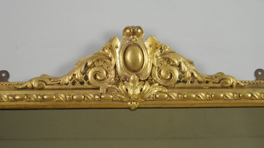 A large Victorian gold leaf gilt overmantel mirror featuring an ornate central crested cartouche, moulding, scroll feet, and arched upper corners. View III