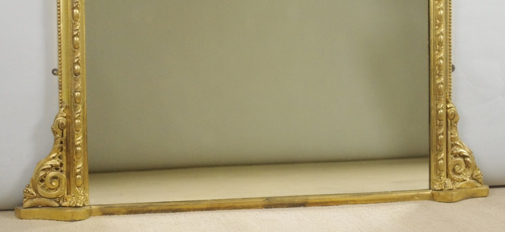 A large Victorian gold leaf gilt overmantel mirror featuring an ornate central crested cartouche, moulding, scroll feet, and arched upper corners. View IX