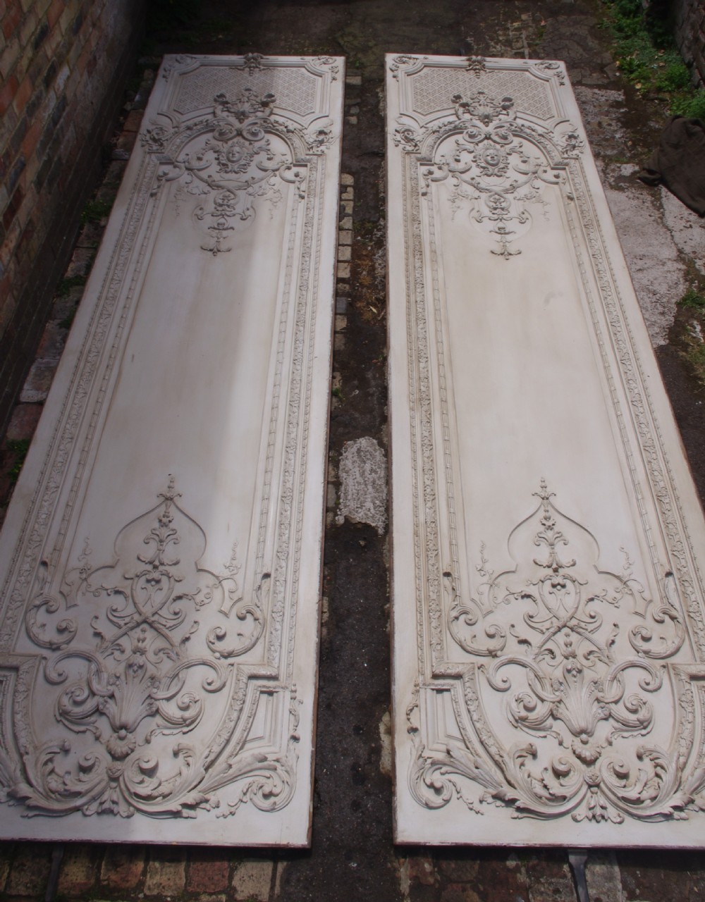 A pair of tall 19th-century French painted wood boiserie wall panels featuring intricate Rococo carved mouldings and foliage motifs in an off-white finish.