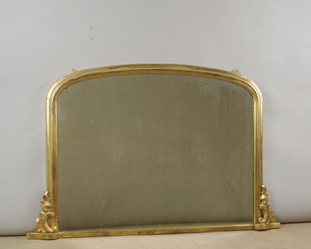 A large Victorian arched overmantel mirror featuring a gilded frame with carved scroll moulding details at the bottom corners.