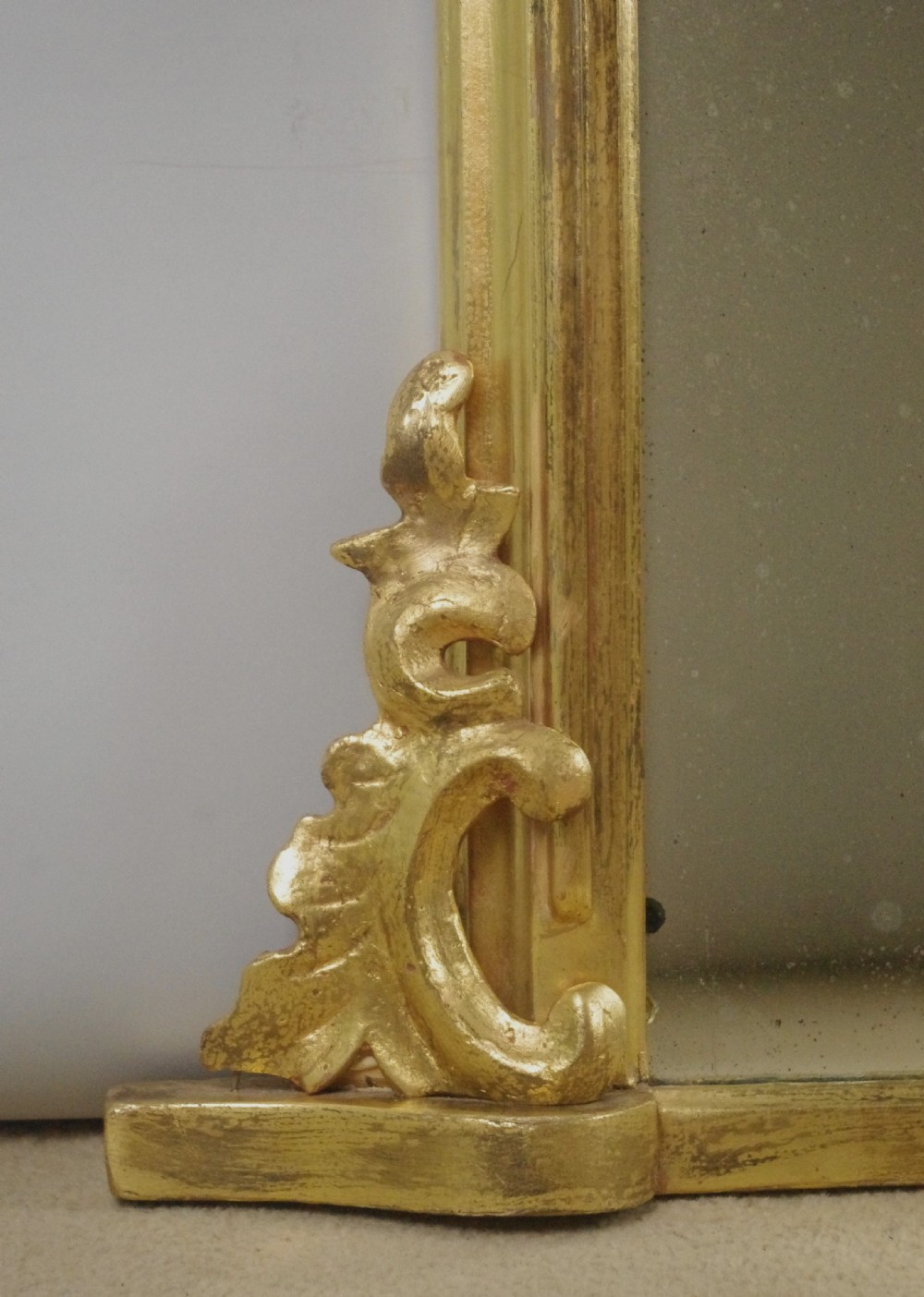 A large Victorian arched overmantel mirror featuring a gilded frame with carved scroll moulding details at the bottom corners. View VI