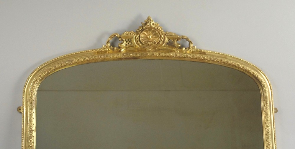 An arched Victorian overmantel mirror featuring a gilded frame with floral mouldings, scrolled side feet, and an ornate top crest. View II