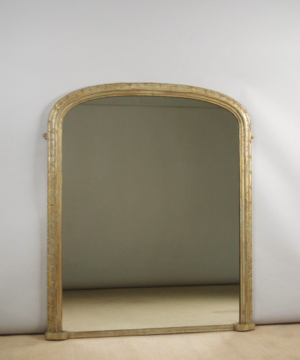 A tall Victorian arched top overmantel mirror featuring a painted wooden frame with geometric carved mouldings and flat base supports.