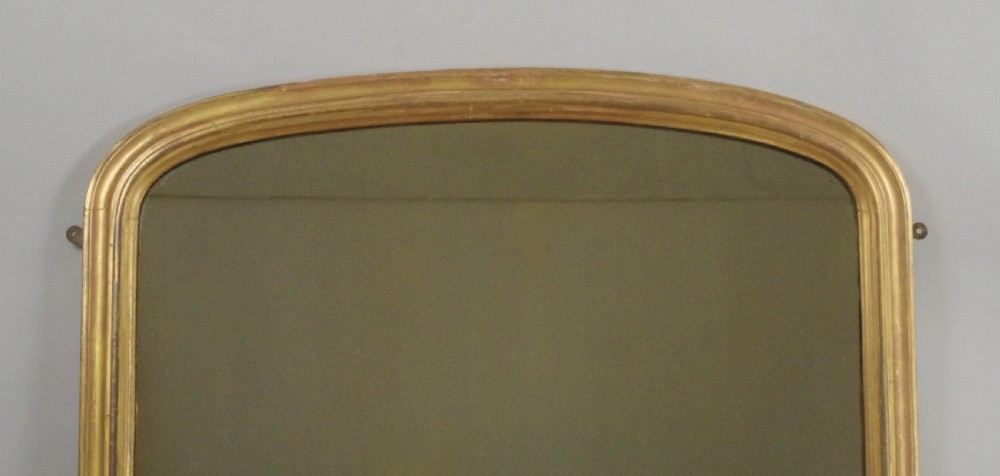 An arched Victorian giltwood overmantel mirror featuring moulded edging and decorative scroll feet at the base. View II