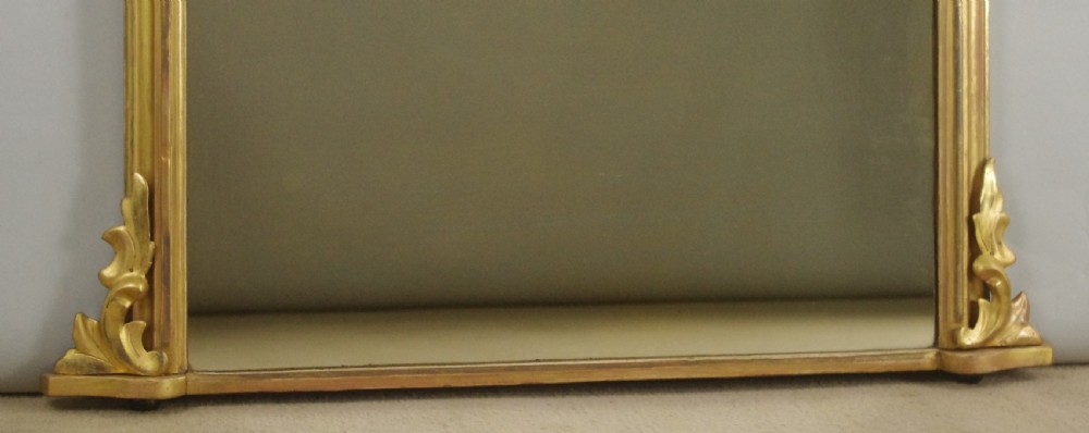 An arched Victorian giltwood overmantel mirror featuring moulded edging and decorative scroll feet at the base. View VII