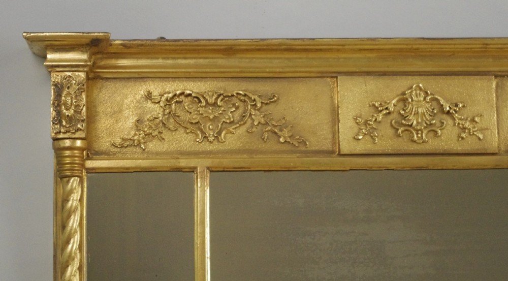 A horizontal Victorian giltwood overmantel mirror with three mirror glass panels, decorative floral relief friezes, and rope-twist side columns. View V