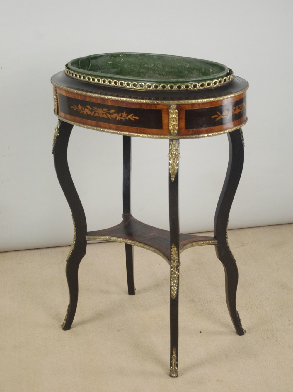 A 19th-century French oval ebonised jardiniere table featuring floral marquetry frieze, gilt-bronze mounts, cabriole legs, and a green metal liner with a pierced brass gallery.