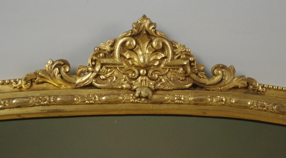 A nineteenth-century arched overmantel mirror featuring a gilded frame with a central ornate crest and decorative corner flourishes. View IV