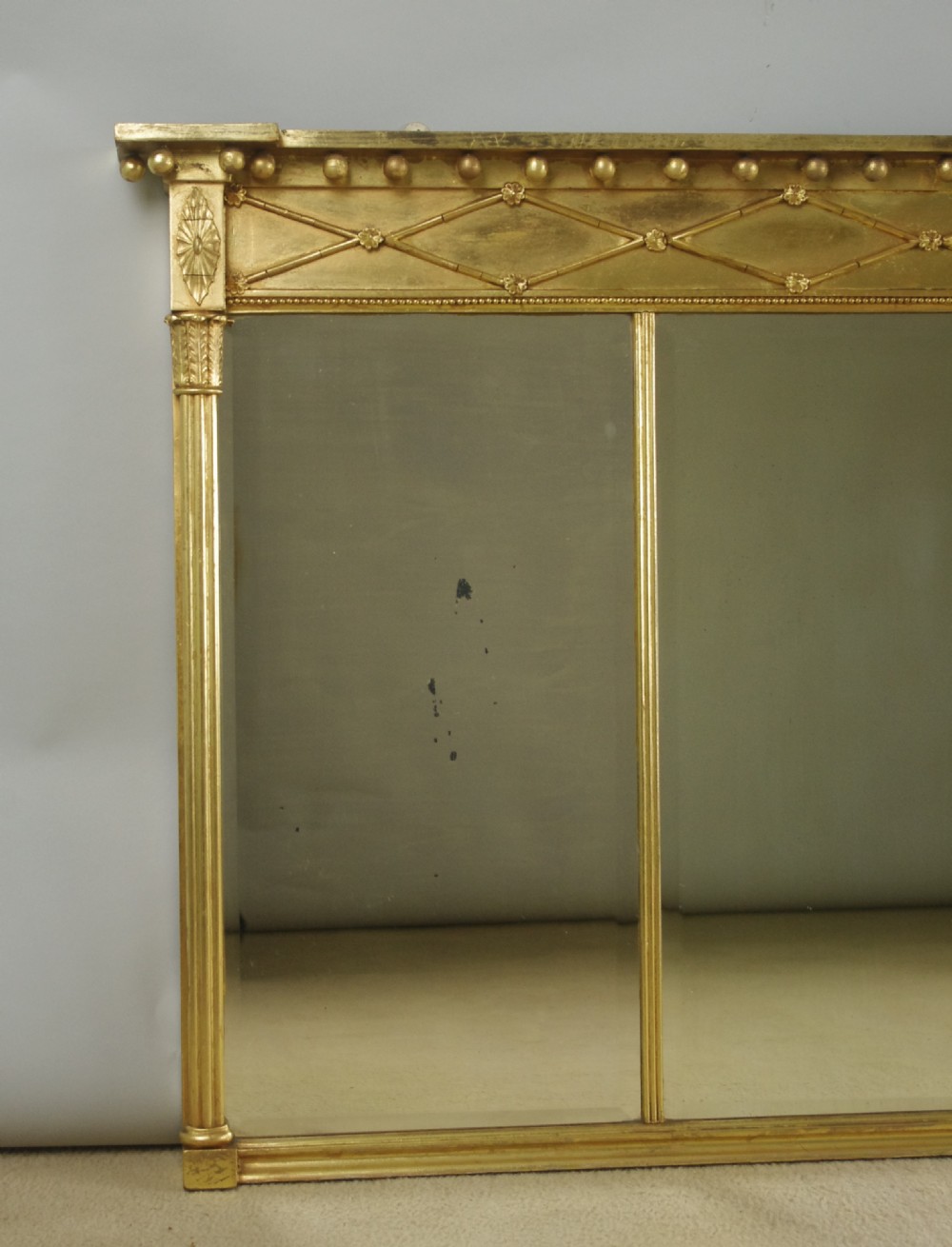 A wide rectangular Victorian giltwood overmantel mirror featuring three mirror plates, fluted side columns, and an ornamental frieze with diamond motifs. View II