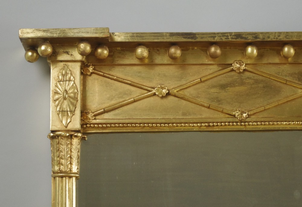 A wide rectangular Victorian giltwood overmantel mirror featuring three mirror plates, fluted side columns, and an ornamental frieze with diamond motifs. View IV