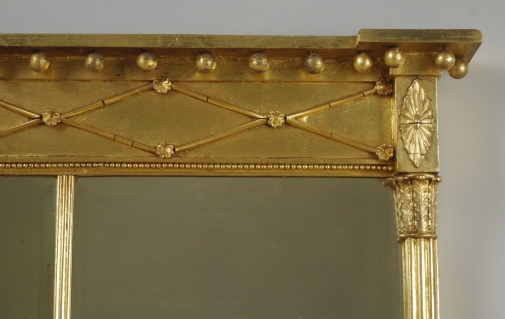 A wide rectangular Victorian giltwood overmantel mirror featuring three mirror plates, fluted side columns, and an ornamental frieze with diamond motifs. View V