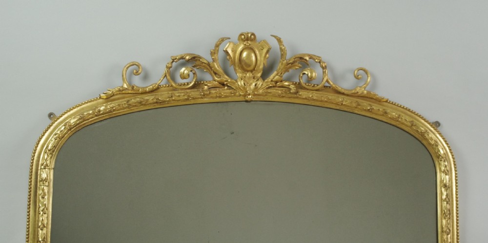 An arched Victorian overmantel mirror featuring a gold giltwood frame with a central scrolled crest motif. View III