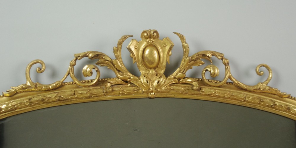 An arched Victorian overmantel mirror featuring a gold giltwood frame with a central scrolled crest motif. View IV