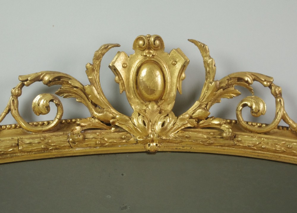 An arched Victorian overmantel mirror featuring a gold giltwood frame with a central scrolled crest motif. View V