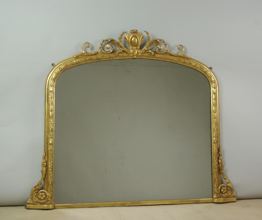 An arched Victorian overmantel mirror featuring a gold giltwood frame with a central scrolled crest motif. View XI
