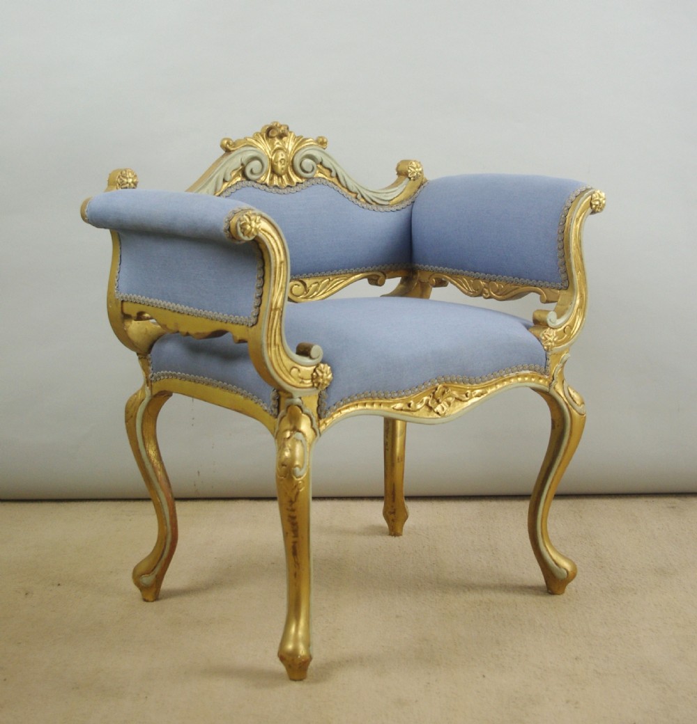 A 19th-century French giltwood occasional chair featuring light blue fabric upholstery, padded scroll arms, carved cresting, and cabriole legs.