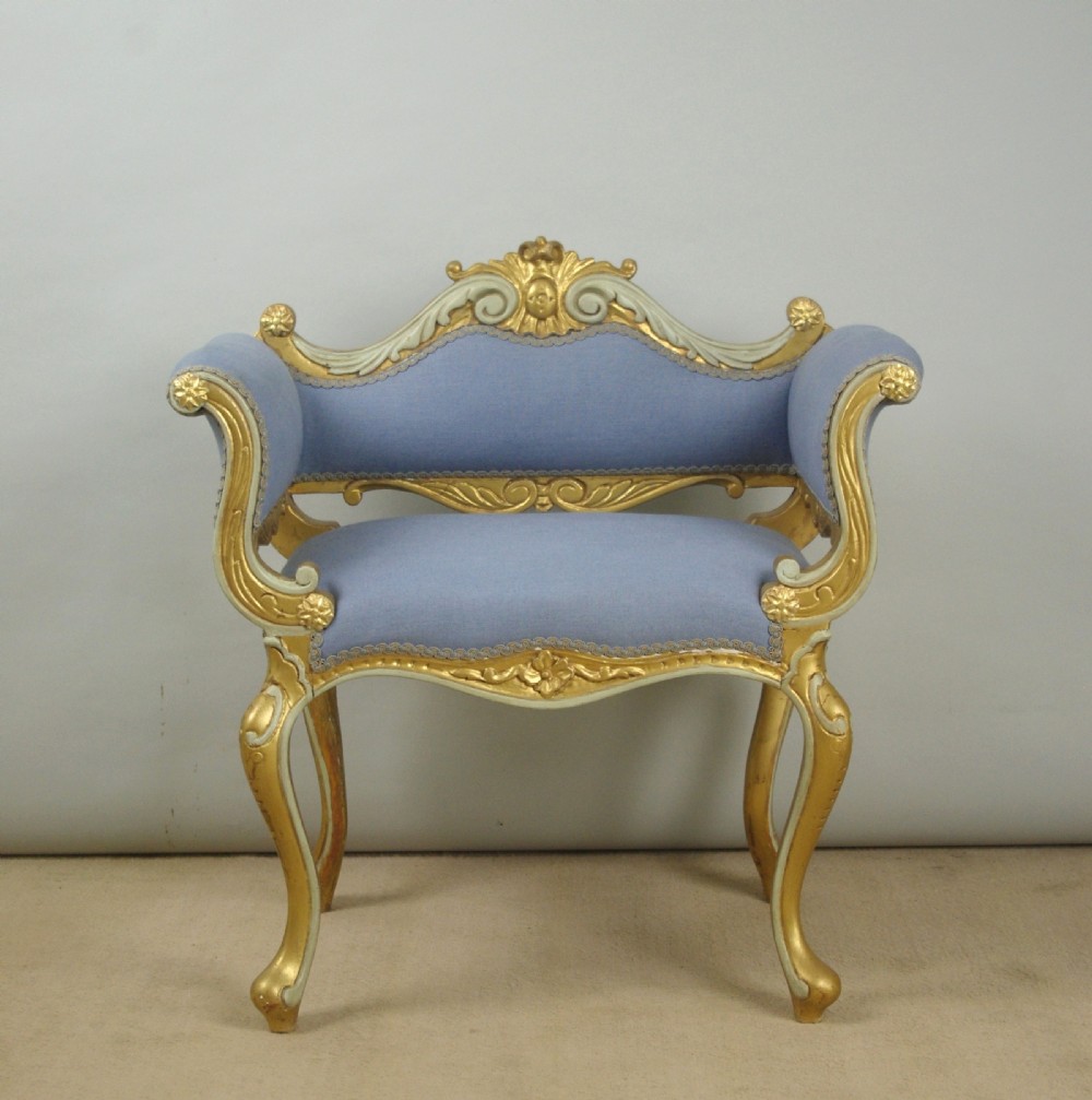 A 19th-century French giltwood occasional chair featuring light blue fabric upholstery, padded scroll arms, carved cresting, and cabriole legs. View II