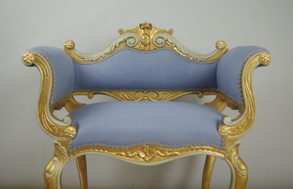 A 19th-century French giltwood occasional chair featuring light blue fabric upholstery, padded scroll arms, carved cresting, and cabriole legs. View III