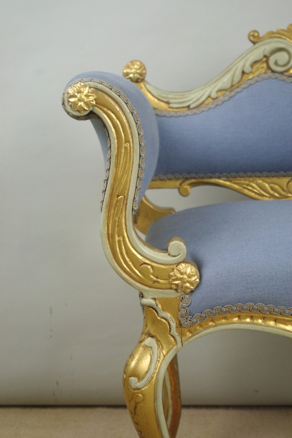 A 19th-century French giltwood occasional chair featuring light blue fabric upholstery, padded scroll arms, carved cresting, and cabriole legs. View V