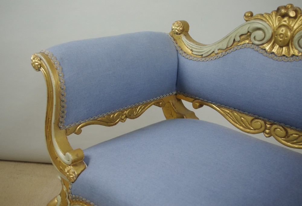 A 19th-century French giltwood occasional chair featuring light blue fabric upholstery, padded scroll arms, carved cresting, and cabriole legs. View X