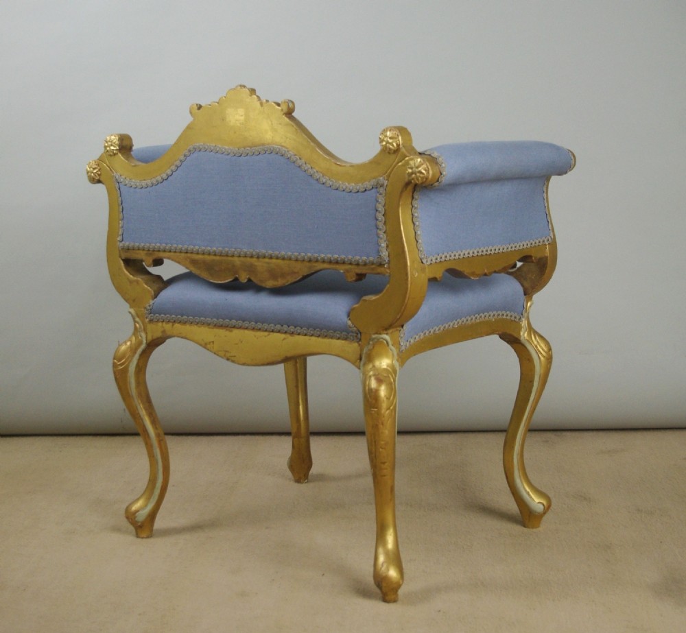 A 19th-century French giltwood occasional chair featuring light blue fabric upholstery, padded scroll arms, carved cresting, and cabriole legs. View XII