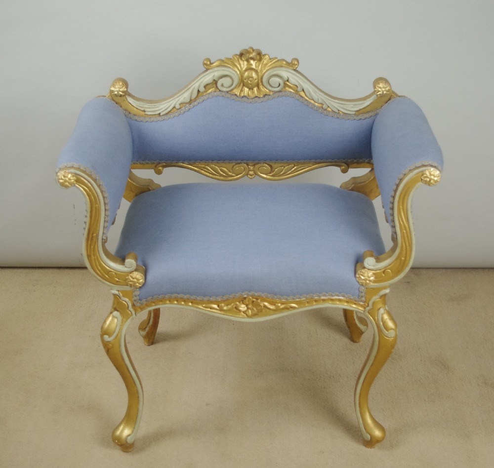 A 19th-century French giltwood occasional chair featuring light blue fabric upholstery, padded scroll arms, carved cresting, and cabriole legs. View XIII