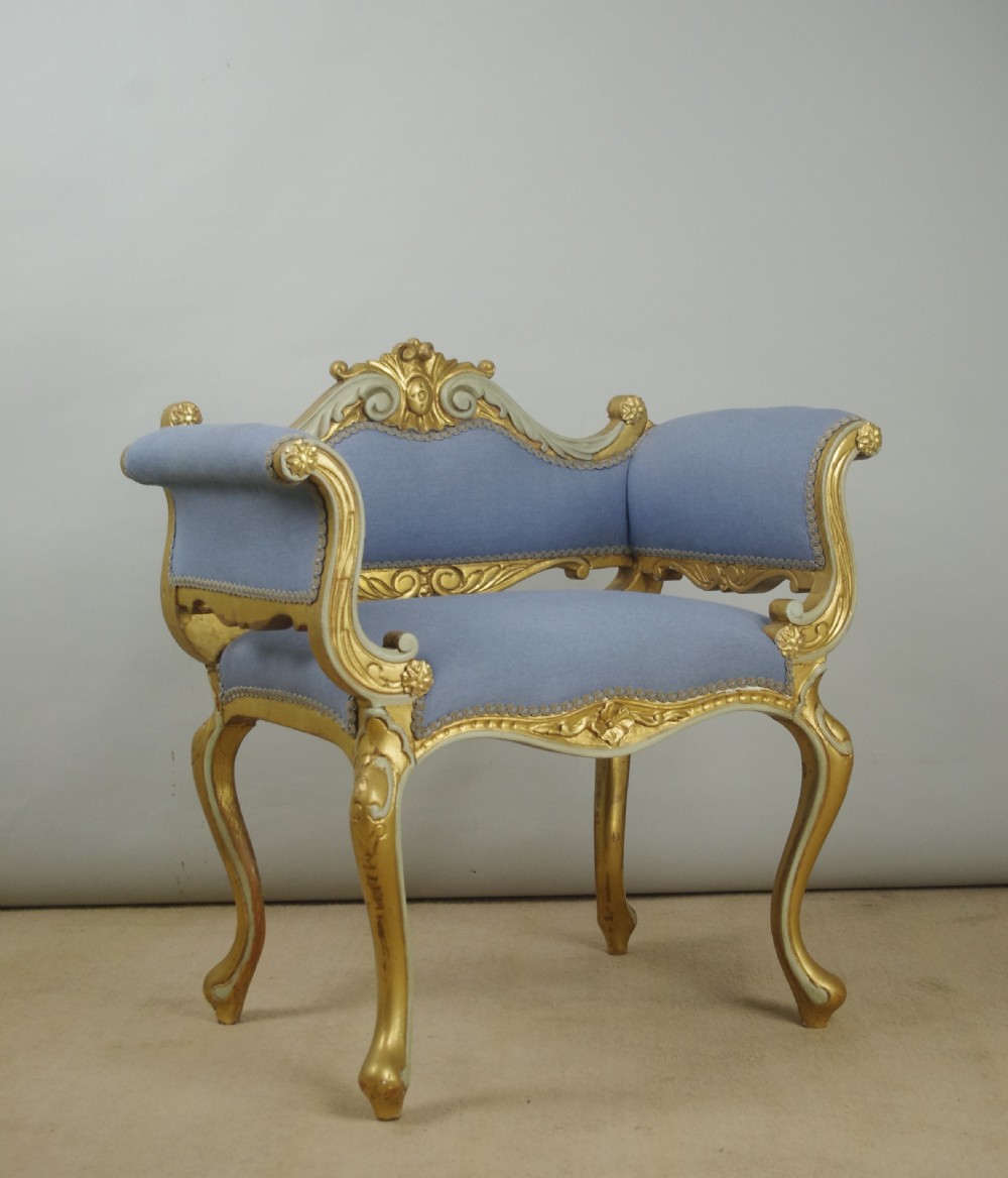 A 19th-century French giltwood occasional chair featuring light blue fabric upholstery, padded scroll arms, carved cresting, and cabriole legs. View XV
