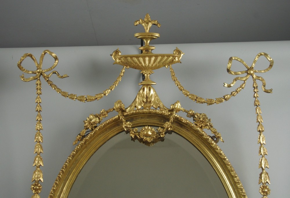 A pair of Victorian giltwood oval wall mirrors topped with urn crestings and ribbon bow swags. View V