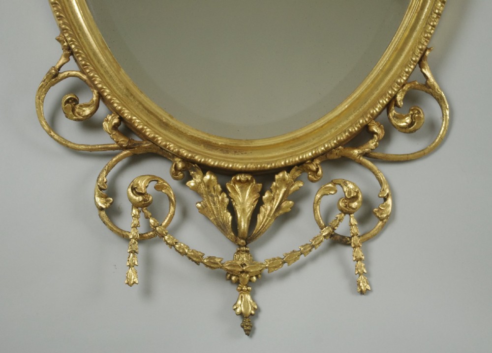 A pair of Victorian giltwood oval wall mirrors topped with urn crestings and ribbon bow swags. View VI