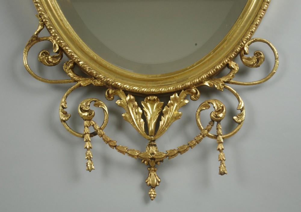A pair of Victorian giltwood oval wall mirrors topped with urn crestings and ribbon bow swags. View VII