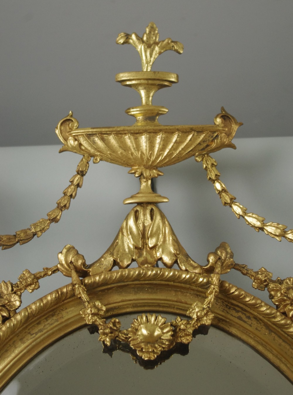 A pair of Victorian giltwood oval wall mirrors topped with urn crestings and ribbon bow swags. View VIII