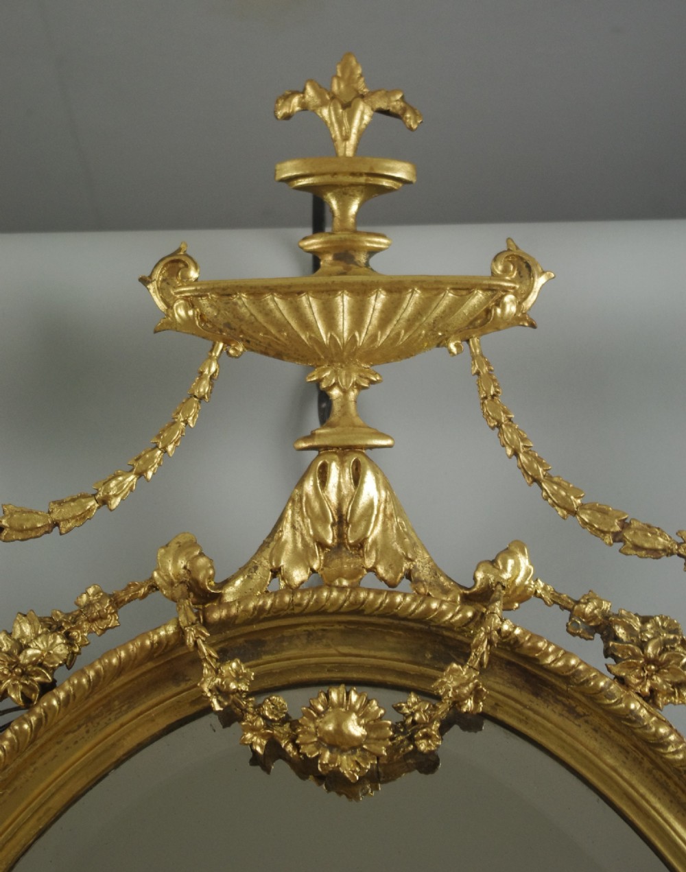 A pair of Victorian giltwood oval wall mirrors topped with urn crestings and ribbon bow swags. View IX