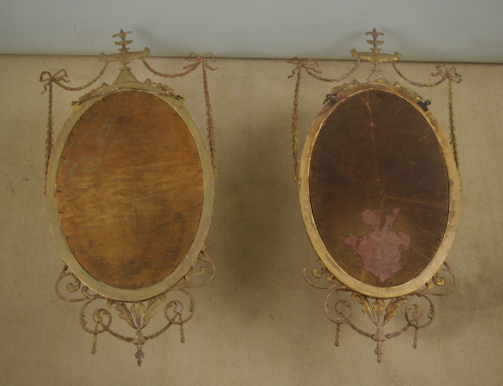 A pair of Victorian giltwood oval wall mirrors topped with urn crestings and ribbon bow swags. View X