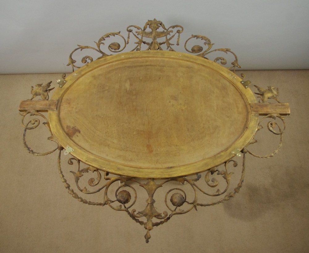 A Victorian giltwood oval wall mirror in the Adam style featuring scrollwork, urn cresting, griffin accents, and floral garlands. View XV