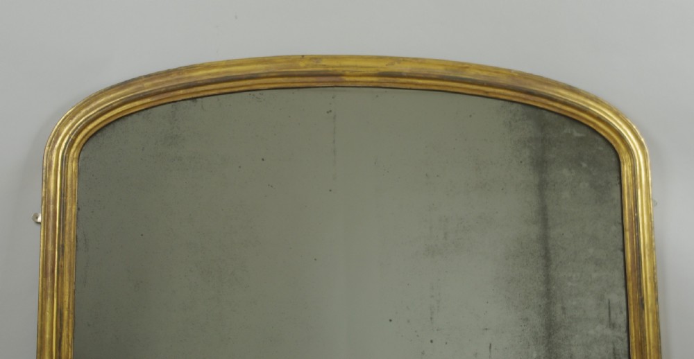 A large Victorian arched overmantel mirror featuring a moulded gold gilt frame and foxed reflective glass. View II