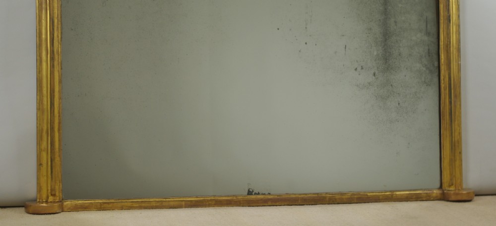 A large Victorian arched overmantel mirror featuring a moulded gold gilt frame and foxed reflective glass. View VII