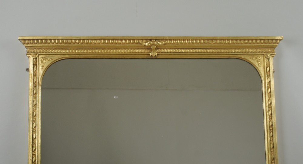 A large Victorian gilt overmantel mirror featuring a rectangular frame with arched upper inner corners, beaded moulding, and scrolled support feet. View II