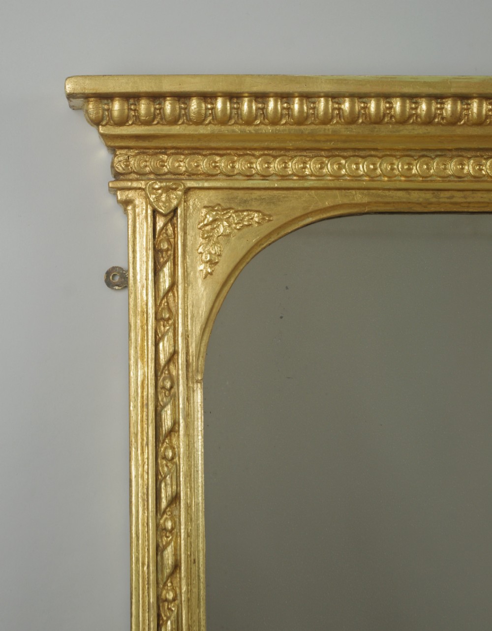 A large Victorian gilt overmantel mirror featuring a rectangular frame with arched upper inner corners, beaded moulding, and scrolled support feet. View III