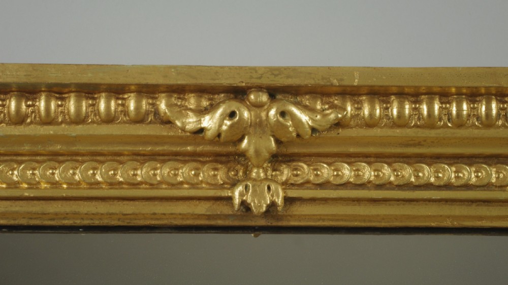 A large Victorian gilt overmantel mirror featuring a rectangular frame with arched upper inner corners, beaded moulding, and scrolled support feet. View V