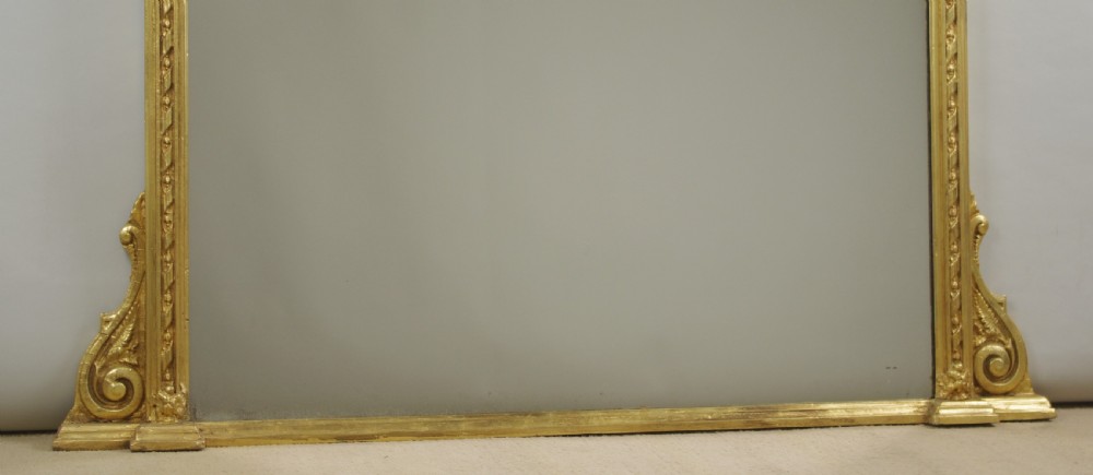 A large Victorian gilt overmantel mirror featuring a rectangular frame with arched upper inner corners, beaded moulding, and scrolled support feet. View VIII