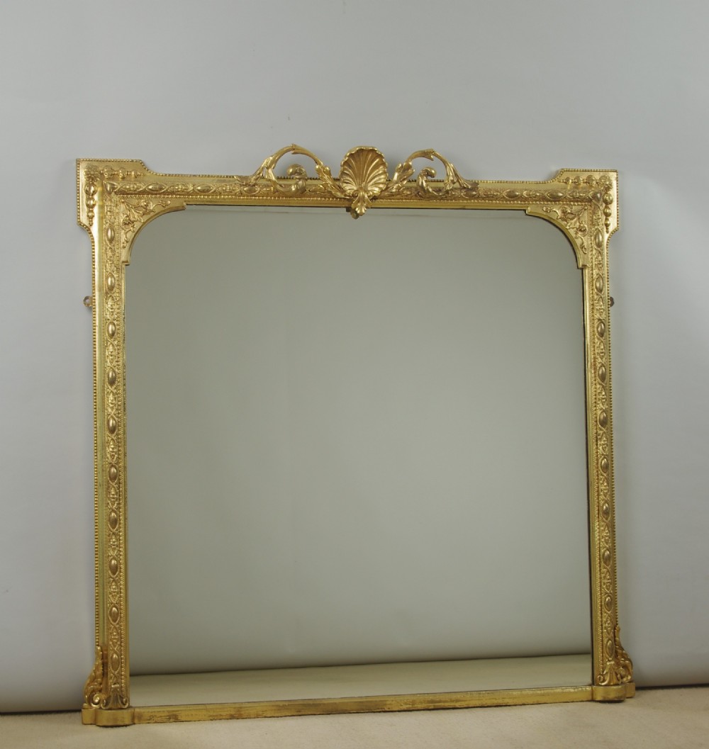 A Victorian giltwood overmantel mirror with an arched frame, central shell crest, and beaded moulding against a neutral backdrop.