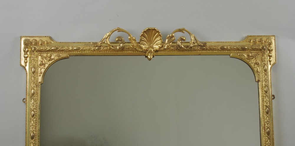 A Victorian giltwood overmantel mirror with an arched frame, central shell crest, and beaded moulding against a neutral backdrop. View II