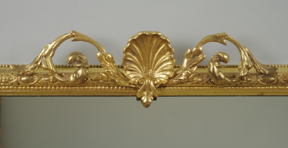 A Victorian giltwood overmantel mirror with an arched frame, central shell crest, and beaded moulding against a neutral backdrop. View V