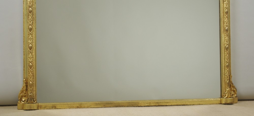 A Victorian giltwood overmantel mirror with an arched frame, central shell crest, and beaded moulding against a neutral backdrop. View VIII