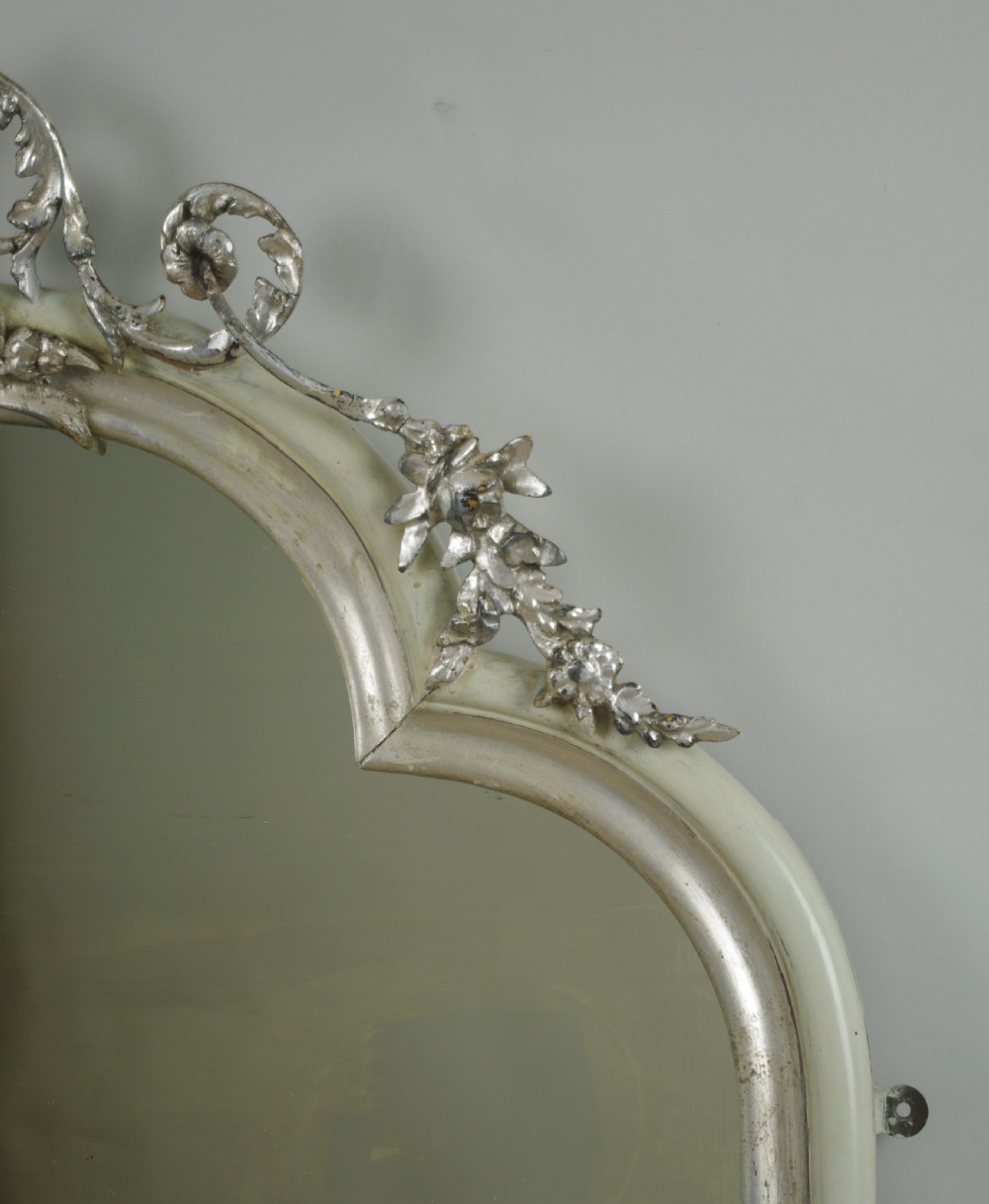 An arched Victorian overmantel mirror featuring a cream painted frame with silvered detailing and an ornate carved mask cresting. View V